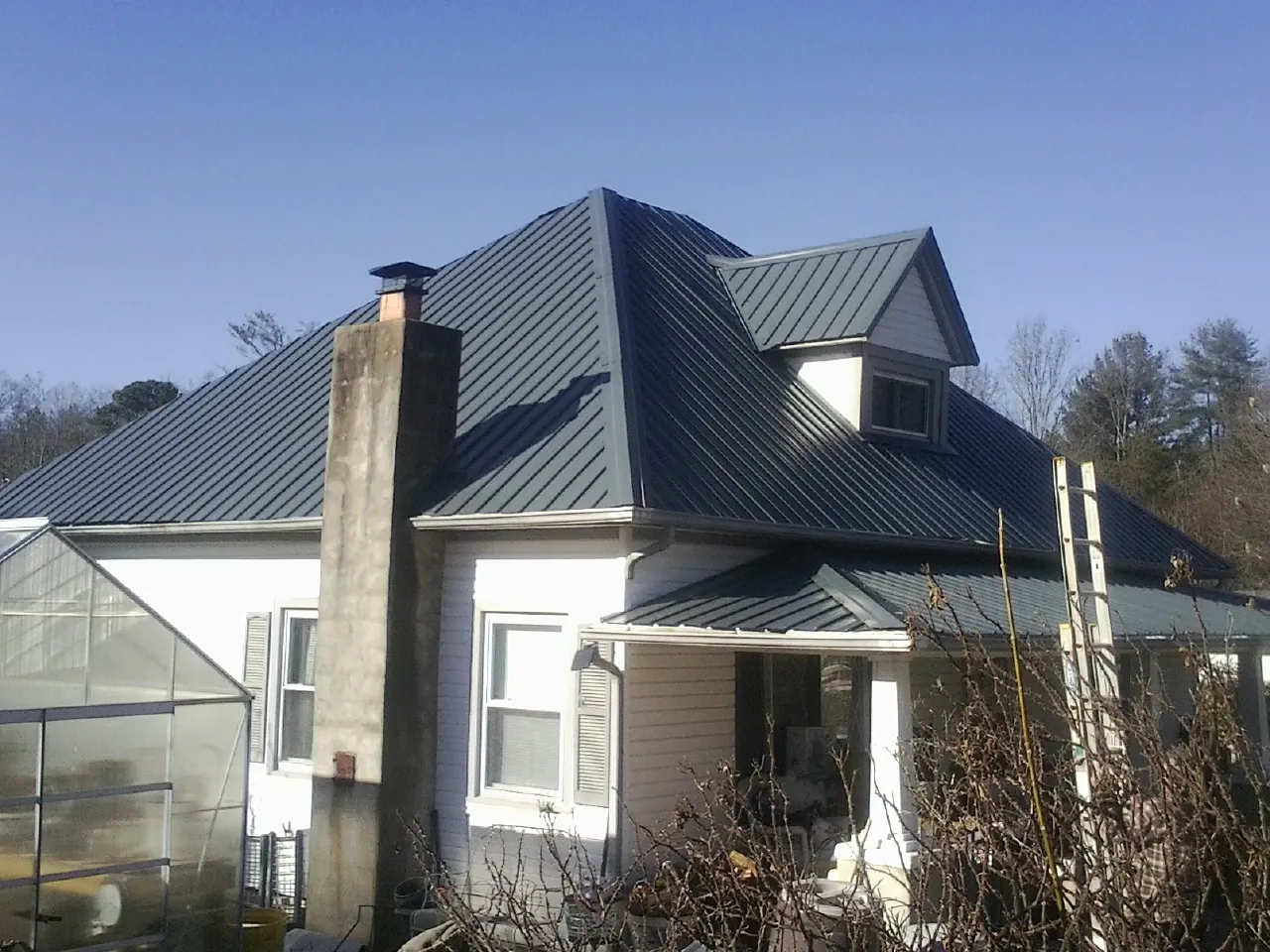 Dark blue standing seam metal roof on a white farmhouse with dormer — Slate & Tile Roof Repair by Roofing Brothers in College Park