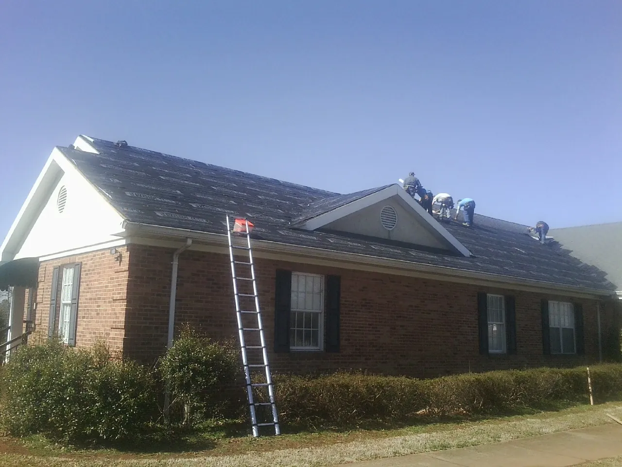 Crew tearing shingles off a brick ranch roof with a ladder set — Emergency Roof Repair work by our crew in College Park