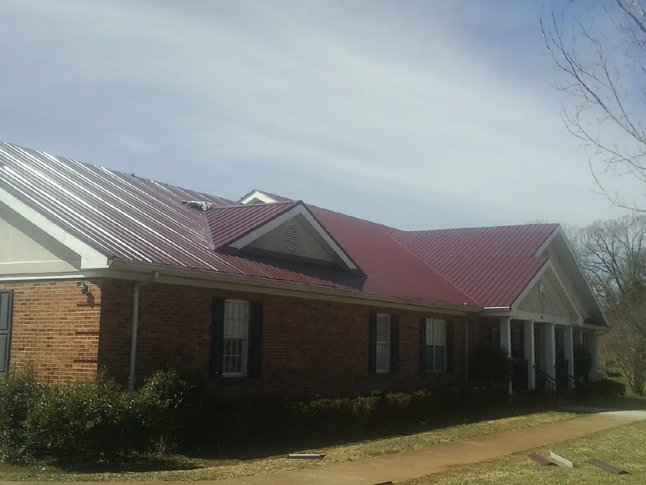 Red metal roof with gabled entries on a long brick building, from a Hail Damage Roof Repair job in College Park