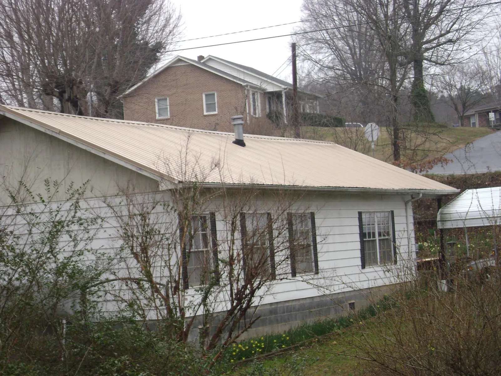 Tan metal roof on a white sided house set into a hillside — Commercial Roofing by Roofing Brothers in College Park